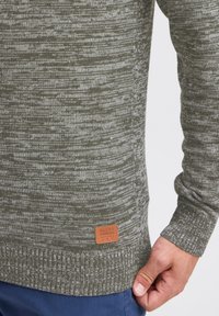 Maglione a maglia verde oliva con un motivo testurizzato, dotato di un'etichetta in pelle marrone con la scritta "BLEND" vicino all'orlo. Maniche aderenti.