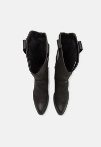 Botas de tobillo de cuero negro con un acabado suave, punta afilada y detalles cosidos. Presentan una textura tejida en el collar y cremalleras laterales.