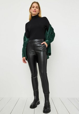 Zwarte geribbelde coltrui, getailleerde zwarte nepleer broek met naden, en zwarte enkellaarzen met zilveren studs.