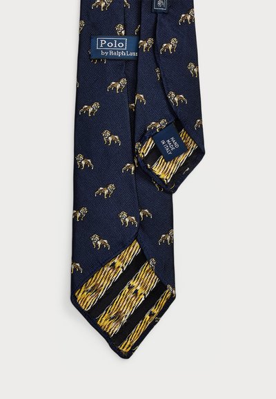 Navy zīda kaklasaite ar zelta lauvas motīviem, ar svītrotu dzeltenu un melnu zīda akcentu galā. Marķējums: "Polo by Ralph Lauren."