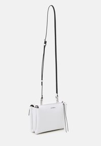 Hvid lædertaske med skulderrem, med en struktureret overflade, der har en aftagelig sort rem og sølvfarvede metal detaljer. Lynlåslommer øverst.