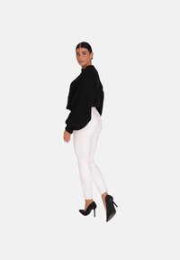 Un pull surdimensionné noir texturé et un jean skinny blanc, présentant une silhouette ajustée et des talons hauts noirs, vu de côté.