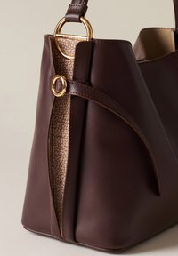 Braune Lederhandtasche mit strukturiertem Design, ausgestattet mit einem goldenen Ringakzent und einem gemusterten Innenraum in Braun und Creme.
