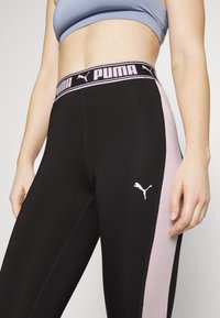 Zwarte sportleggings met roze zijpanelen. Heeft een brede tailleband met het PUMA-logo en een klein roze logo op het onderbeen. Rekbaar, aansluitend ontwerp.