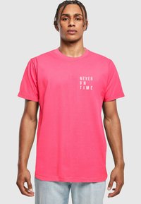 T-shirt di cotone rosa con maniche corte e scollatura a girocollo, con testo stampato bianco "NEVER ON TIME" posizionato verticalmente sul davanti.