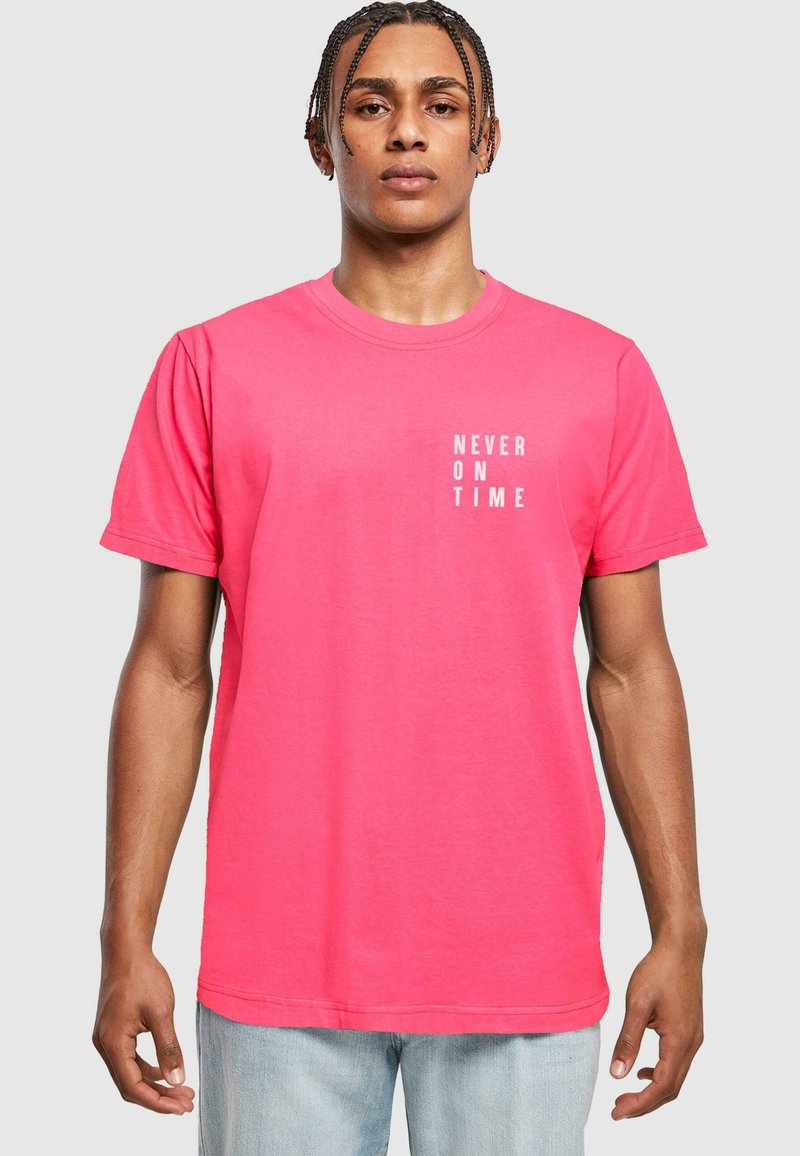 T-shirt di cotone rosa con maniche corte e scollatura a girocollo, con testo stampato bianco "NEVER ON TIME" posizionato verticalmente sul davanti.