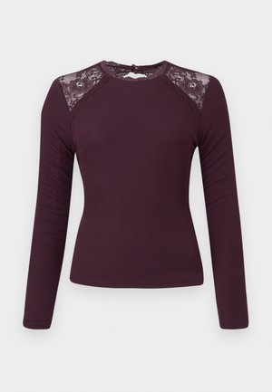 Langsleeve, ribbeltop in diep bordeaux met kantaccenten op de schouders en een ronde halslijn, voorzien van een knoopsluiting aan de achterkant.