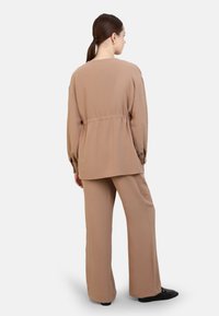 Ensemble beige en deux pièces comprenant un haut ample ettexturé avec une taille froncée et un pantalon à jambes larges, le tout en tissu doux et fluide.