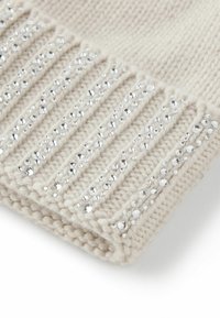 Dziana czapka typu beanie w jasnobeżowym kolorze z ozdobnymi srebrnymi cekinami wzdłuż prążkowanego brzegu, charakteryzująca się miękką teksturą i zaokrąglonym kształtem.