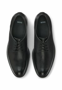 Scarpe eleganti in pelle nera con una texture liscia, design con lacci, punta rotonda e logo sottile sulle sole interne. Stile e silhouette minimalista.