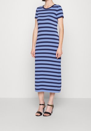 Mujer que lleva un vestido midi a rayas horizontales en azul y azul marino, con mangas cortas y sandalias negras de tacón alto con correas en el tobillo.