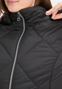 Sort boblejacket med høj krave, sølv lynlås og diamantquiltet mønster. Glat tekstur med en blank finish.