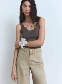 Top de tânără cu dungi maro, cu dantelă la margini, asortat cu pantaloni bej cu talie înaltă. Brățara florală din material alb accentuează încheietura.