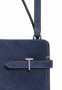 Borsa a spalla in denim blu scuro con cuciture gialle a contrasto, dotata di un accento in metallo argentato e una chiusura a patta con un dettaglio a "T".