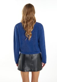 Blauer, flauschiger Pullover mit langen Ärmeln, Rundhalsausschnitt und cropped Fit. Kombiniert mit einem schwarzen Leder-Minirock mit unsichtbarem Reißverschluss.