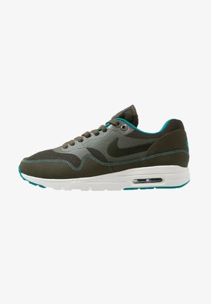 Baskets Nike vert foncé et gris avec accents turquoise, semelle blanche avec coussin d'air visible, et lacets à l'avant, vues de profil.