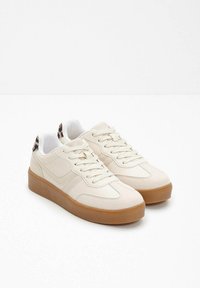 Un paio di sneaker beige basse con suole in gomma e dettaglio in stampa leopardata sul tallone, esposte su uno sfondo bianco.