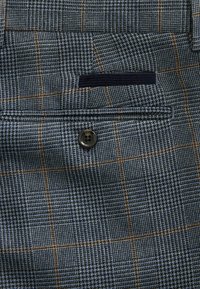 Blue and gray patterned fabric featuring a houndstooth design, with orange accents. Includes a buttoned pocket detail on the front.