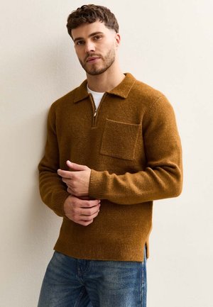 Pull en tricot marron avec un col zippé quart, col classique et une poche poitrine. Présente des fentes sur les côtés, une texture douce et des poignets côtelés.