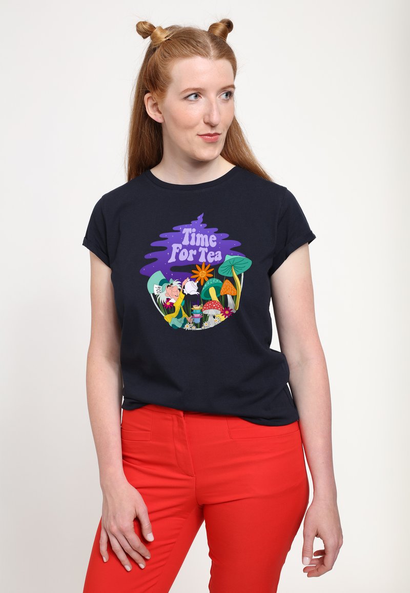 Granatowy t-shirt z kolorowym nadrukiem "Czas na herbatę", przedstawiającym postacie, kwiaty i grzyby; stylizowany z czerwonymi spodniami.