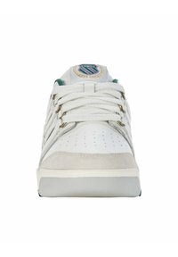 Sneaker bianca con punteggiature sulla punta, accenti in suede e dettagli verdi. Presenta un'etichetta con logo sulla linguetta e lacci piatti. Suola in gomma.