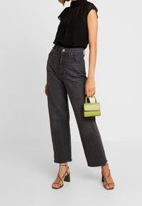 Mustat läpinäkyvät puserot, joissa on puffihihat. Korkeavyötäröiset tummanharmaat suorat farkut. Vihreä pikkulaukku. Remmiset vihreät korkokengät.