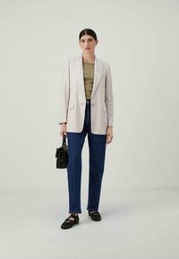 Blazer beige chiaro su misura, top verde, jeans in denim blu, borsa nera e ballerine nere; tessuto liscio, design strutturato e vestibilità classica.