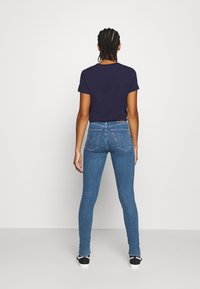 Jeans ajustados de denim azul con una cinturilla alta y bolsillos traseros distintivos, combinados con una camiseta azul marino. La tela tiene un aspecto suave y ceñido.