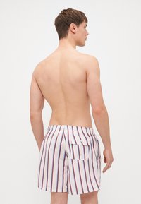 Férfi úszónadrág fehér alapon függőleges piros és kék csíkokkal. Hátsó zsebének patentos zárása van, valamint rugalmas derékpántja.