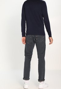 Marineblått stickat tröja med ribbade manschetter, kombinerad med mörkgrå jeans. Vita sneakers med gröna detaljer på hälen och uppvikta benslut.