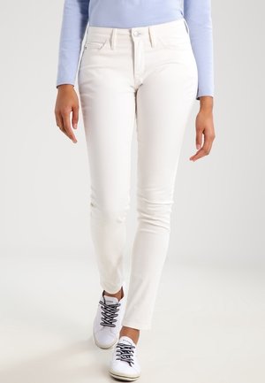 Jean blanc moulant en denim, avec une texture lisse, un design à cinq poches et une fermeture à bouton. Associé à des baskets blanches.