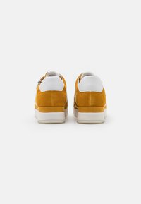 Yellow suede sneakers with white leather accents, featuring a padded collar and a contrasting rubber sole. Zipper detail on the side.