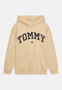 Felpa beige con tasca a marsupio frontale, caratterizzata da un logo "TOMMY" ricamato in blu navy e accenti di branding rosso, bianco e blu. Tessuto morbido.