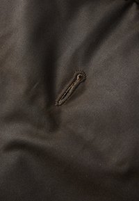 Aproximação de um tecido escuro com um botão em forma oval vertical, cosido com fio da mesma cor.