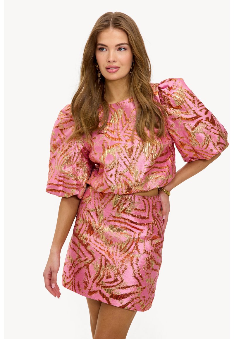 Tenue bicolore rose comprenant un haut texturé avec des manches bouffantes et une jupe assortie, toutes deux ornées d'un motif doré métallique.