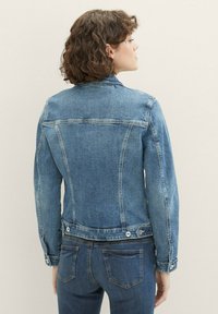 Giacca di jeans in azzurro chiaro, con un design aderente, dettagli di cucitura sottili, polsini con bottoni e due tasche posteriori.