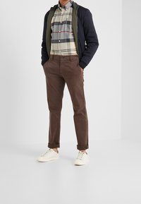 Pantaloni di cotone marroni, camicia a quadri grigia e bianca, giacca a zip blu navy, sneakers bianche, con risvolti e design slim fit.