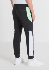 Zwarte sportieve joggers met groene en witte zijpanelen, elastische tailleband en geribde boorden. Voorzien van een logo op de achterkant.