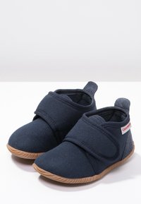 Navy canvas kengät, joissa on tarranauha, pyöreä kärki ja vaaleanruskea kumipohja. Ominaisuuksiin kuuluu teksturoitu kangas ja pieni logotunnus sivussa.