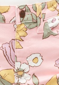 Ροζ ύφασμα με πολύχρωμο λουλουδάτο μοτίβο, που παρουσιάζει πράσινα φύλλα, λευκά και κίτρινα λουλούδια, και ένα καφέ κουμπί κοντά σε θηλιά ζώνης.