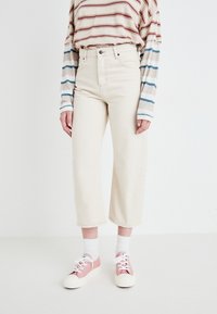Beige vidde jeans med høy midje, sammen med en stripete langermet skjorte i krem, blått og rødt, samt rosa joggesko.