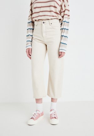 Beige wijde jeans met een hoge taille, gecombineerd met een gestreept shirt met lange mouwen in crèmekleur, blauw en rood, en roze casual sneakers.