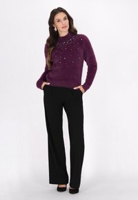 Lilla fuzzy sweater med perleaccenter ved halsen, parret med sorte vide bukser og sorte hæle.