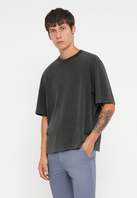 Mørkegrå oversized t-skjorte i myk stoff med rund hals og korte ermer, kombinert med lyseblå bukser. Har synlige sømmer.