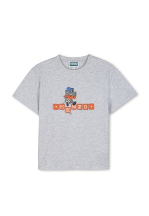 T-shirt Kenzo gris clair avec un chien de dessin animé portant une casquette bleue et un t-shirt orange, marchant sur des dés orange au centre.