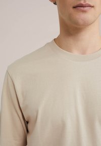 Béžové bavlněné tričko s kulatým výstřihem, hladkým povrchem a žebrovaným límcem, s krátkými rukávy a jednoduchým, klasickým designem.