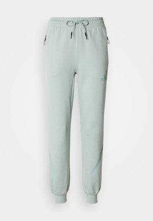 Pantalon de survêtement vert clair en tissu doux avec taille élastique, cordon de serrage et poches zippées. Présente un logo discret et des accents subtils.