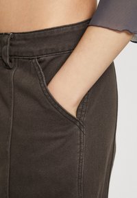 Jupe en denim marron avec poches latérales, détail de couture visible et taille mi-haute. Le tissu a une texture lisse avec un léger stretch.