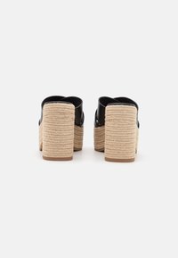 Sandalias de plataforma negras con correas anchas y tacones de tejido beige texturizado. Los tacones son altos, con un aspecto de fibra natural y un acabado suave.