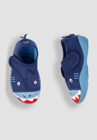 Béguins pour bébé de couleur bleu marine sur le thème des requins avec une tige en tissu extensible, présentant un visage de requin souriant, des dents blanches et des semelles en caoutchouc bleu.